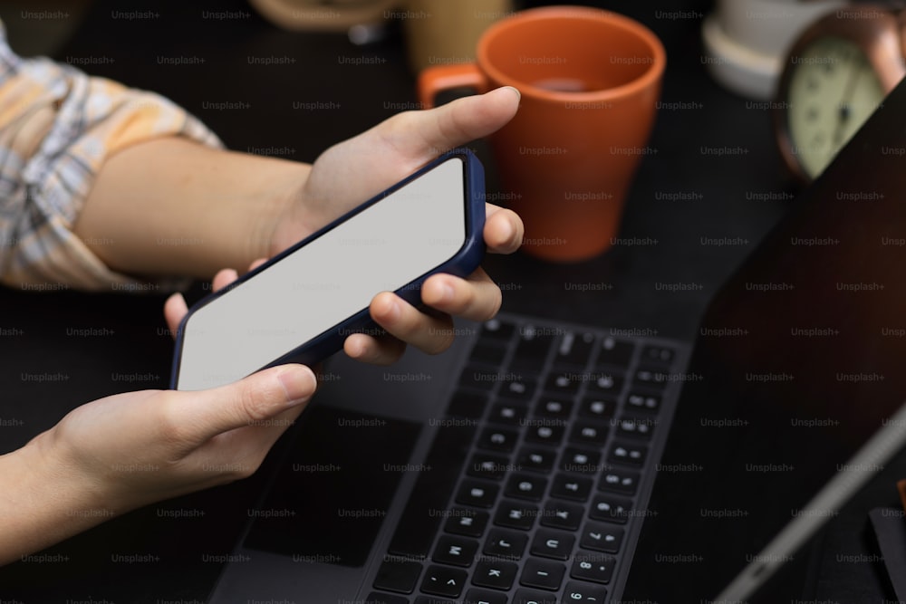 Close-up, jovem hipster sentada no espaço de trabalho moderno, usando mensagens de smartphone seus amigos, maquete de tela do telefone, tablet desfocado e fundo de decoração