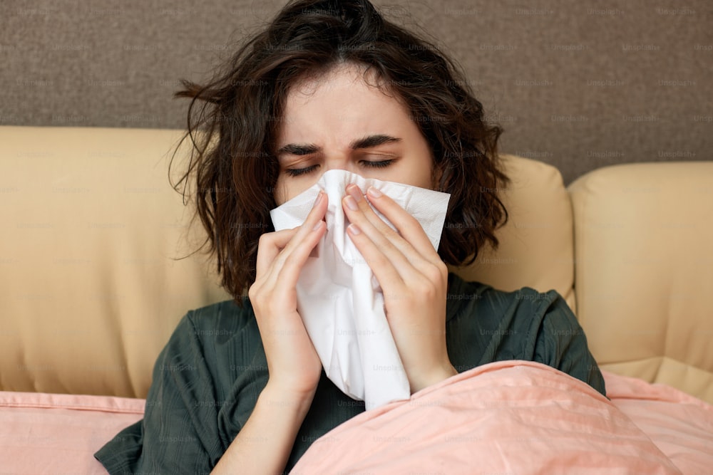sick woman sneezing and covering nose with paper napkin, close-up