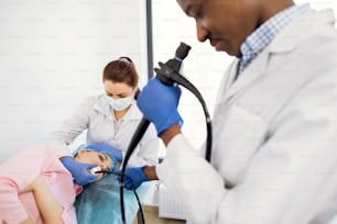 Professional nurse and male afro-american gastroenterologist conducting endoscopy for young female patient at the hospital. Healthcare and medicine.