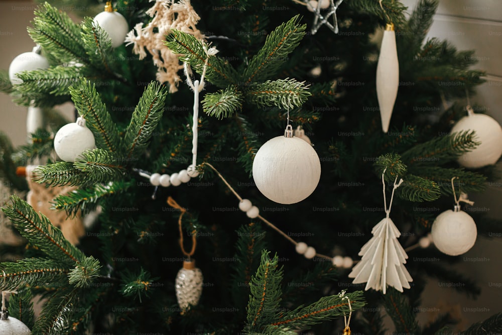 Adornos modernos del árbol de Navidad boho, adornos blancos, guirnalda de madera, luces navideñas de cerca. Ambiente festivo decorado en una habitación escandinava decorada. Elegante decoración navideña