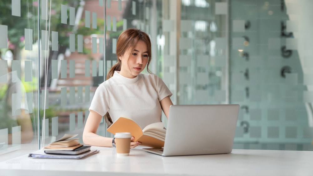 Bella donna d'affari asiatica seduta in ufficio con un laptop e un notebook.