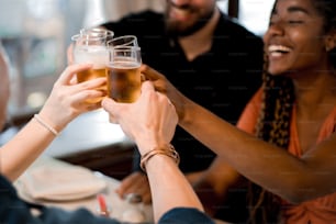 Gruppo di diversi amici che brindano con bicchieri di birra mentre si godono un pasto insieme in un ristorante. Concetto di amici.