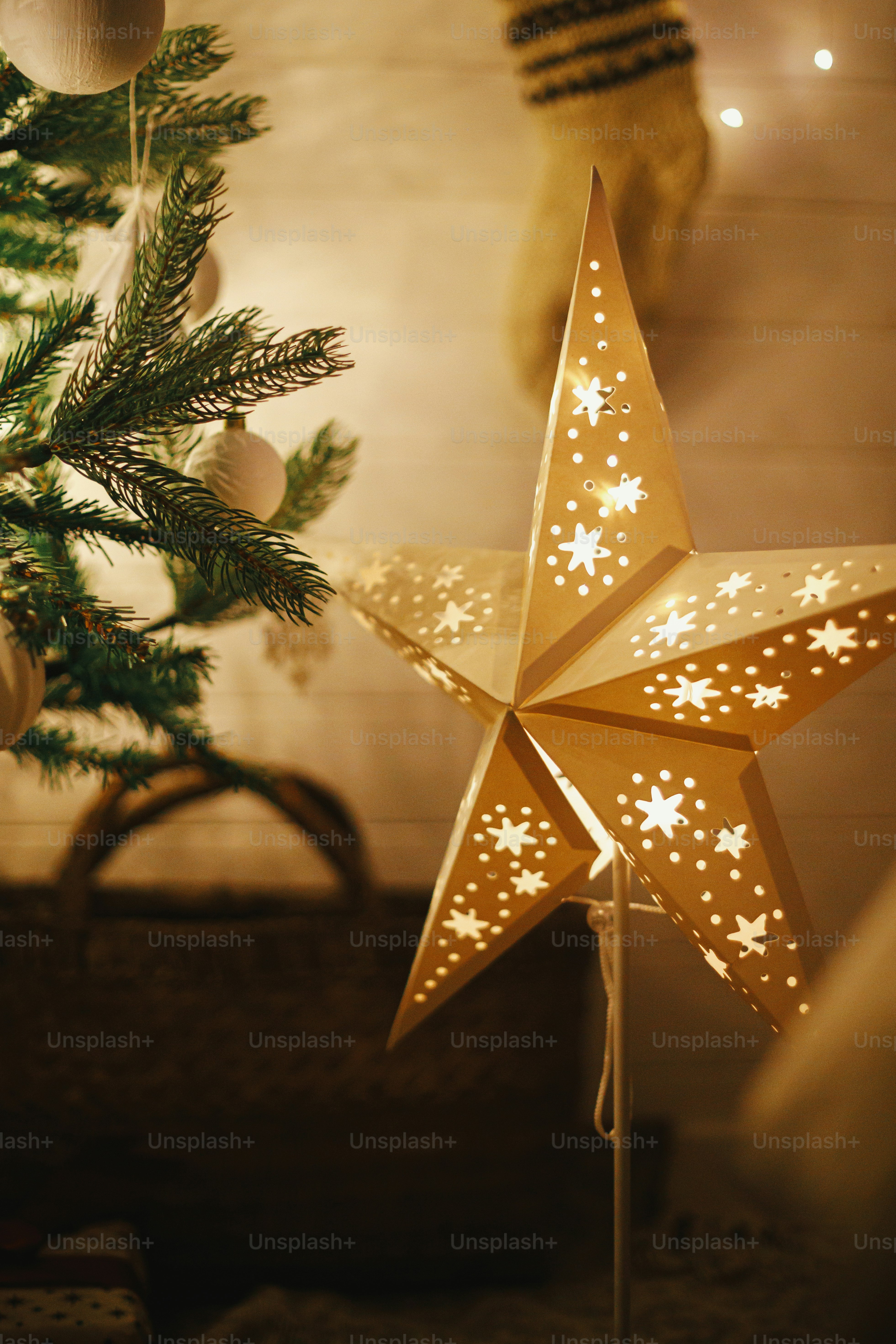 Frohe Weihnachten! Stilvoller Weihnachtsstern, Baum mit weien Kugeln,  Boho-Ornamente, goldene Lichter und Geschenke im stimmungsvollen Abendraum.  Festliches skandinavisches Zimmer am Abend. Magische Zeit. Platz fr Text.  Foto  Bild zum Thema Weihnachten