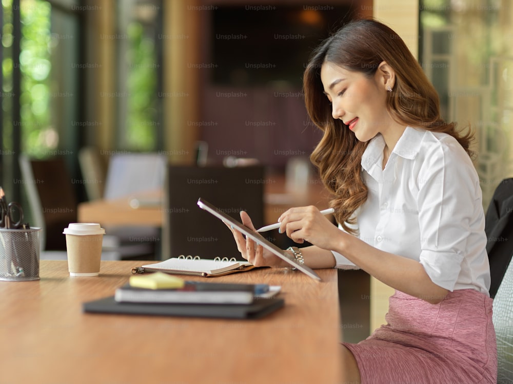 Mujer de negocios que verifica las existencias de la tableta digital, idea de publicidad de la lista en la tableta en el escritorio de trabajo de la oficina