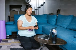 Kurviges lateinamerikanisches Mädchen mit Smartphone kniet im Wohnzimmer in Lateinamerika, Plus-Size-Frau