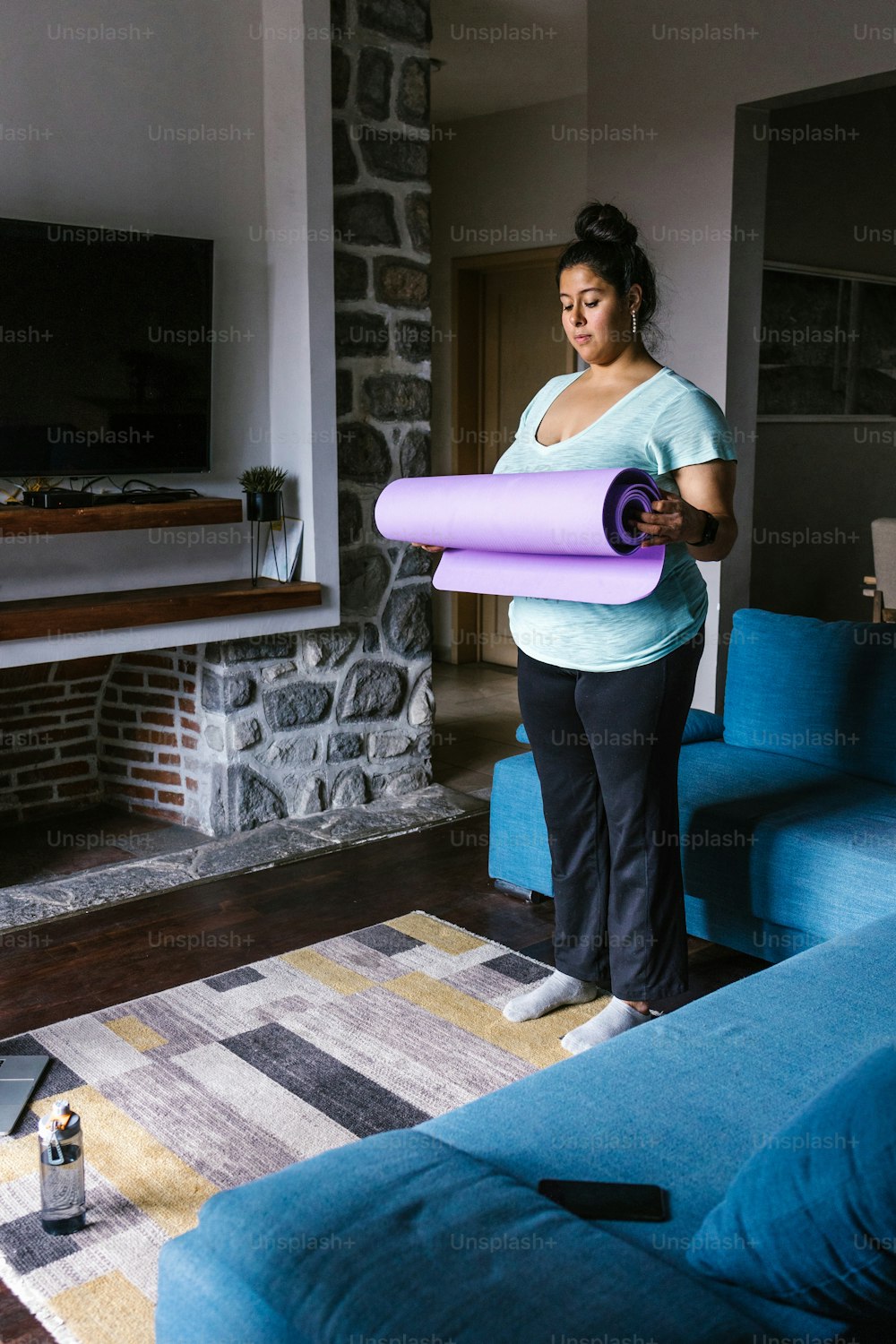 Young plus size latin woman holding a mat standing in the living room in Latin America