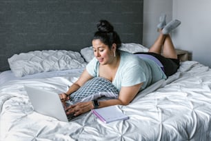 Mujer latina con curvas acostada en la cama usando la computadora en América Latina, mujer de talla grande
