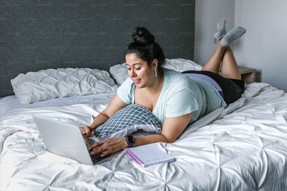 Mulher latina curvilínea deitada na cama usando o computador na América Latina, fêmea plus size