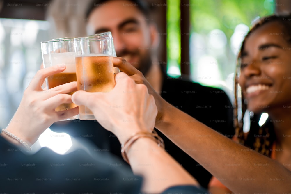 Group of diverse friends toasting with beer glasses while enjoying time together at a bar or pub. Friends concept.