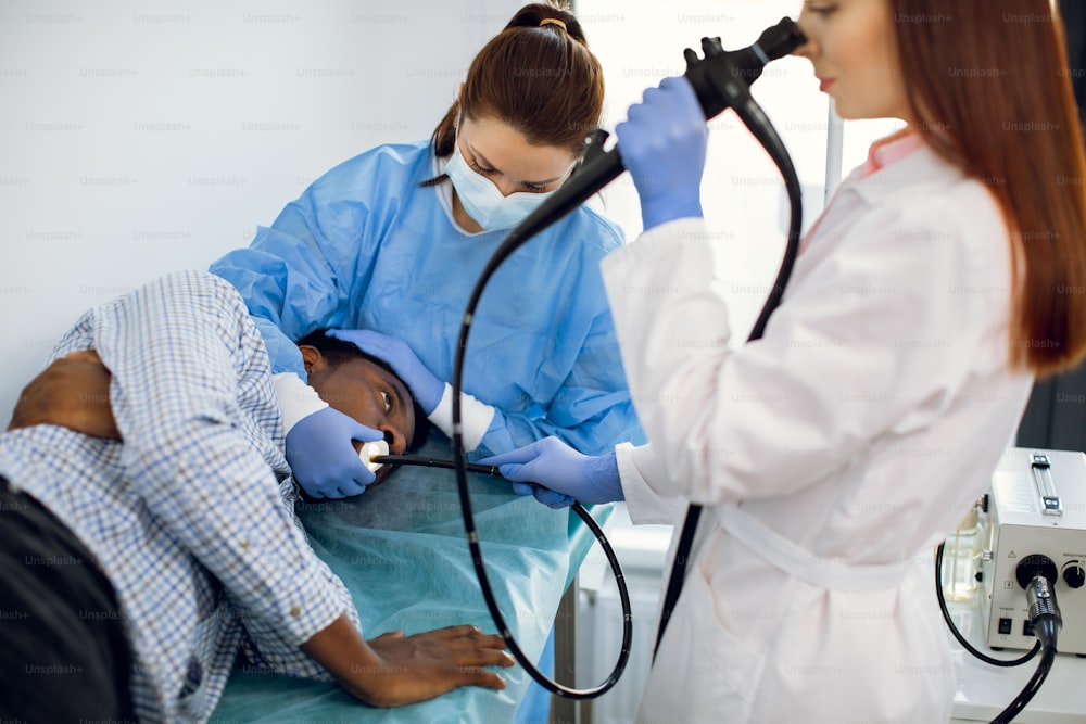 Male African patient having endoscopy in modern clinic. Two professional female Caucasian doctors conducting fibrogastroduodenoscopy procedure.