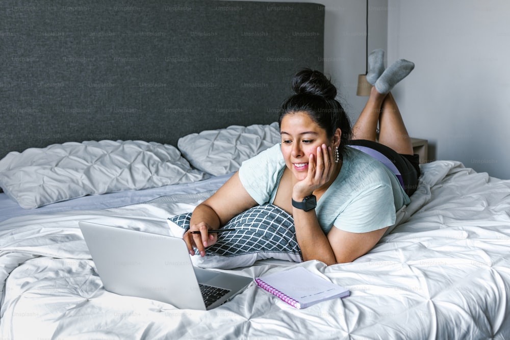 Femme latine bien roulée allongée sur le lit à l’aide d’un ordinateur en Amérique latine, femme de grande taille