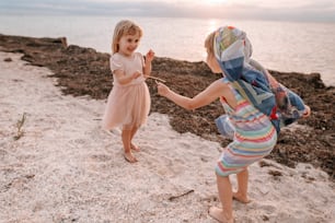 Two little girls having fun time playing fighting with wands on the beach at summer sunset