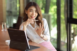 Happy businesswoman showing ok hand sign while sitting at work place, cheerful pretty worker