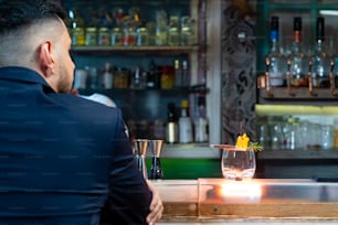 Retrato de un hombre caucásico guapo sentado en la barra del bar sosteniendo un vaso de whisky con hielo y disfruta bebiendo una sabrosa bebida alcohólica del barman en el club nocturno. Celebración de la fiesta de vacaciones de la vida nocturna y concepto de pequeña empresa