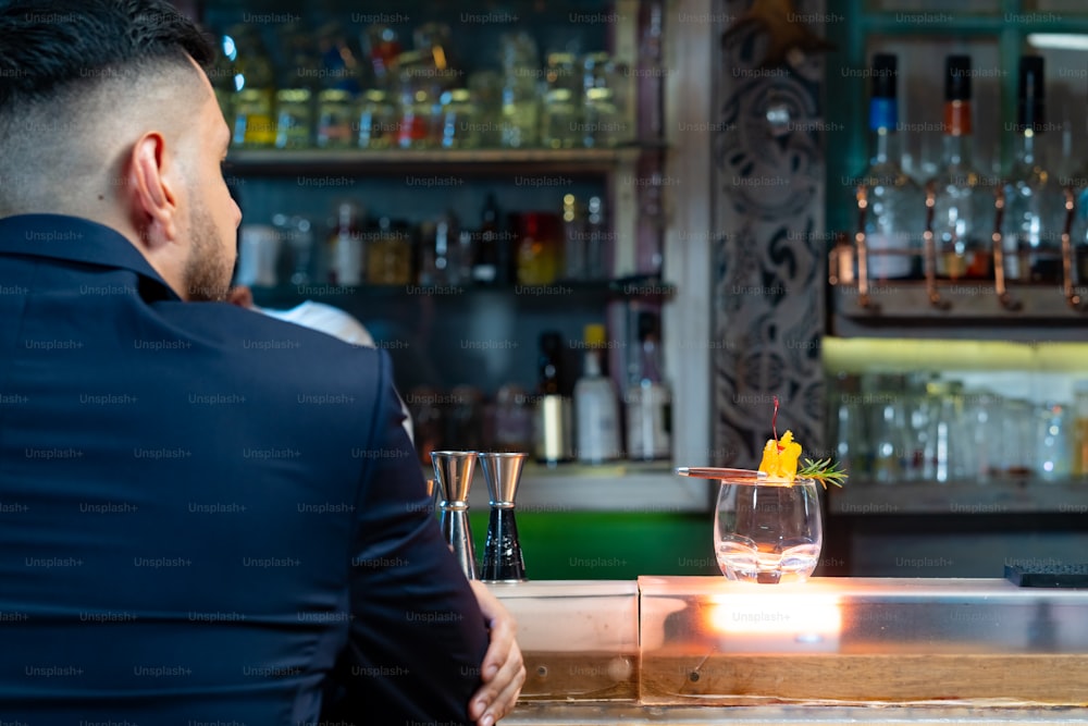 Ritratto di bell'uomo caucasico seduto al bancone del bar che tiene il bicchiere di whisky con ghiaccio e si diverte a bere una gustosa bevanda alcolica dal barista in discoteca. Celebrazione della festa di festa della vita notturna e concetto di piccola impresa