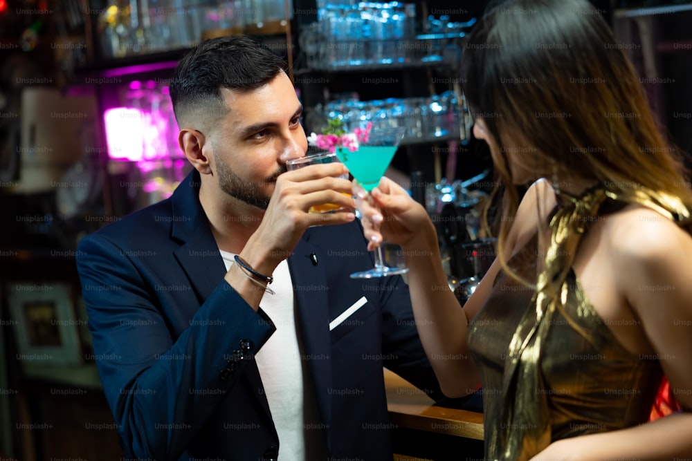 バーカウンターに立って、ナイトクラブでアルコールカクテルを飲みながらボーイフレンドと話しているアジア人女性。バーカウンターでカクテルグラスを飾るミックスアルコール飲料を準備する男性バーテンダーのミクソロジスト