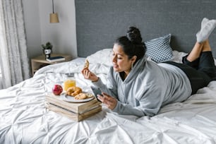 Mujer hispana gordita que desayuna en la cama mientras usa el teléfono en América Latina, mujer de talla grande