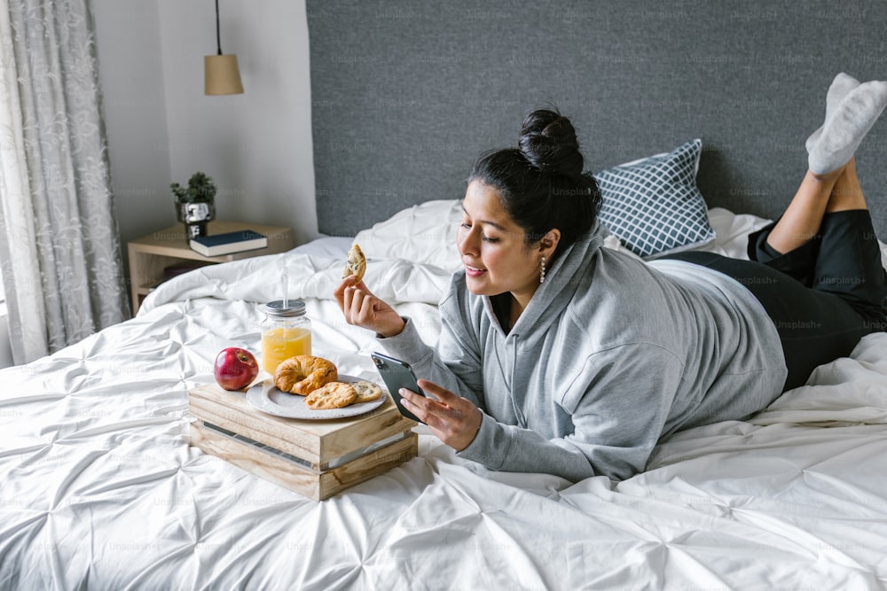 Pummelige hispanische Frau frühstückt im Bett, während sie in Lateinamerika telefoniert, plus Größe weiblich