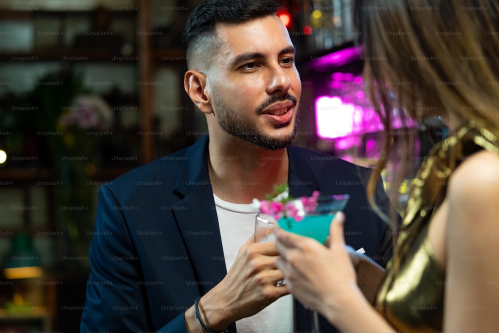 Asiatische Frau, die an der Bartheke steht und mit ihrem Freund einen alkoholischen Cocktail im Nachtclub trinkt. Männlicher Barkeeper Mixologe, der alkoholische Mixgetränke mit dekoriertem Cocktailglas an der Bartheke zubereitet
