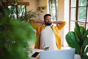 A young man with laptop and coffee working indoors, home office concept.