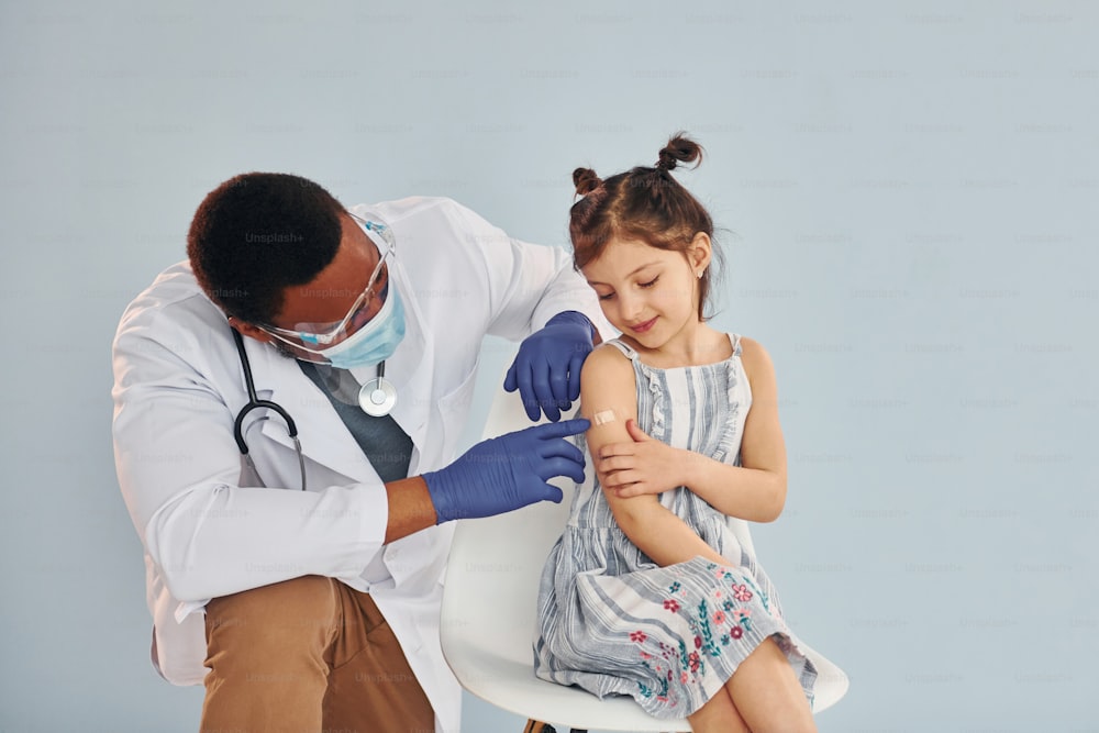 Joven médico afroamericano administrando una inyección a una niña en el hospital.