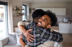 A young happy adult brothers in kitchen indoors at home, hugging.