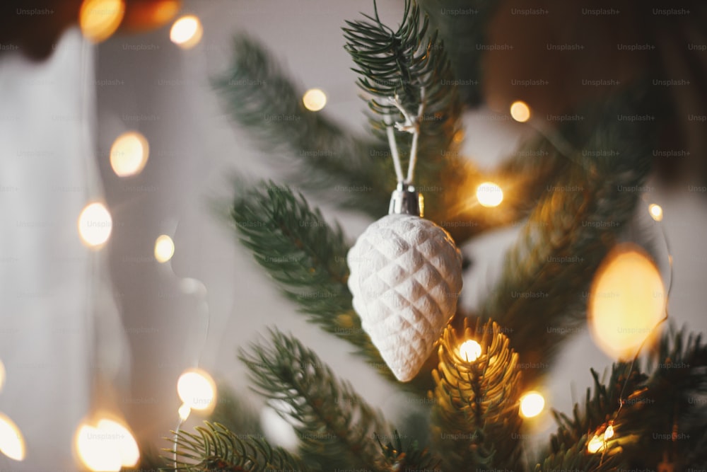 현대적인 크리스마스 트리 장식품, 흰색 싸구려 및 황금빛 크리스마스 조명 보케가 닫힙니다. 텍스트를 위한 공간입니다. 분위기 있는 축제 장식 스칸디나비아 객실. 세련된 크리스마스 장식