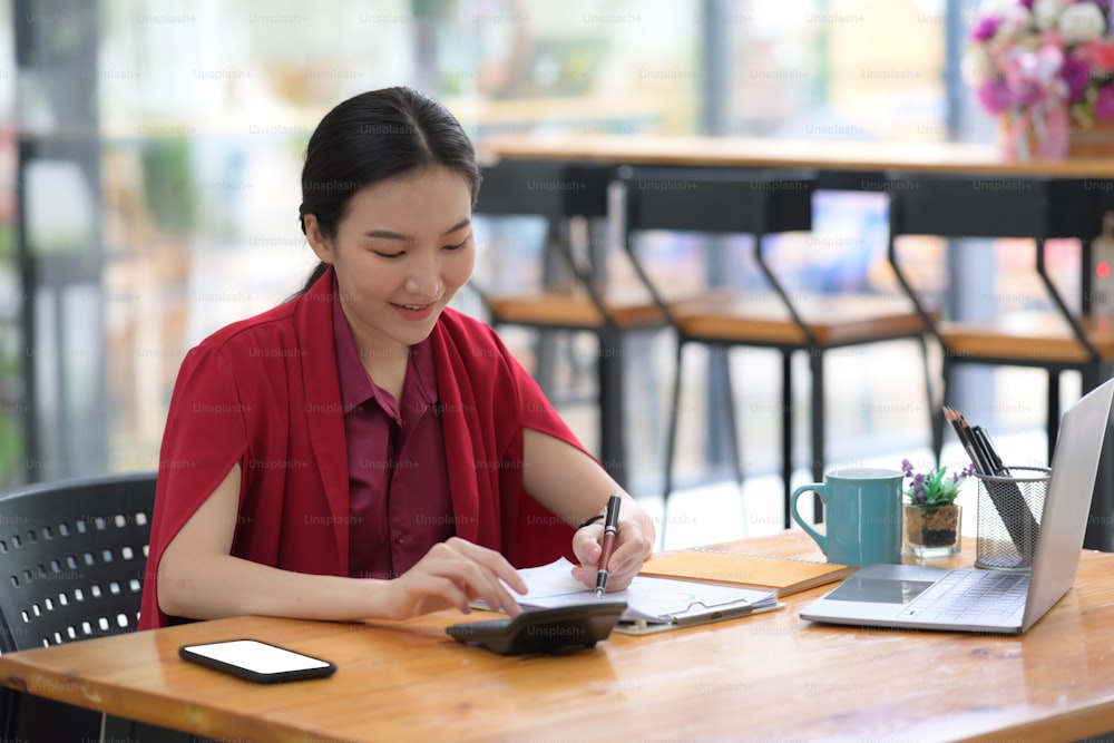 Beautiful businesswoman using calculator and analyzing reports.