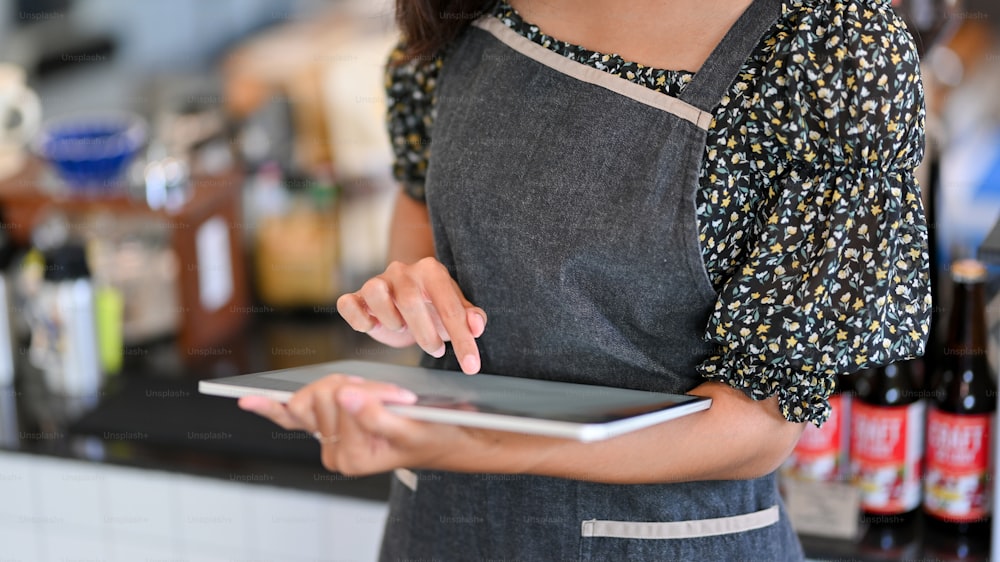 Image recadrée d’une jeune femme barista prenant une commande sur une tablette dans un café