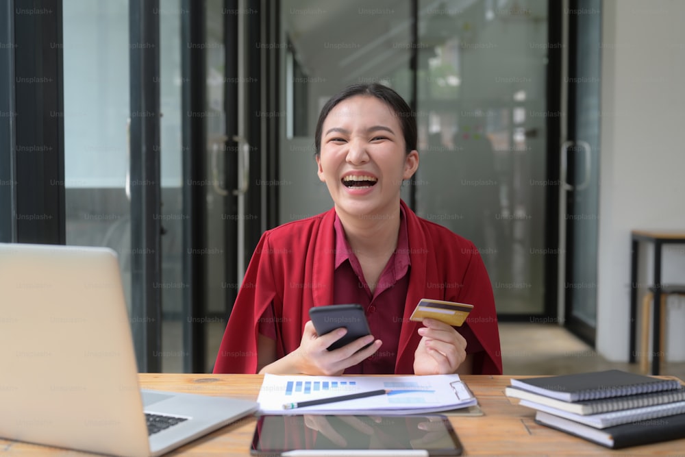 Cheerful Asian woman using mobile phone and credit card for making shopping online.