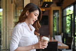 Peaceful businesswoman standing in office and drinking hot coffee.