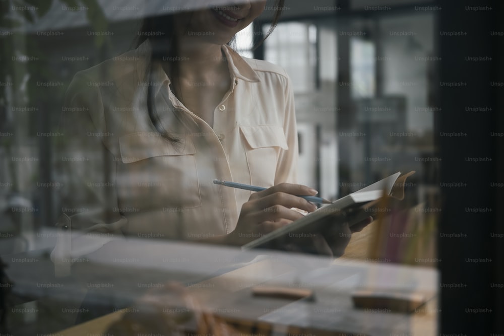 View through window of businesswoman holding pen and making note on notebook.