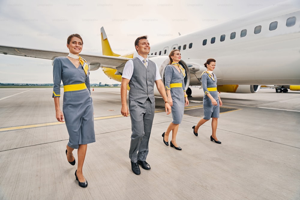 Full-length portrait of a smiling steward and three stewardesses in uniforms going along the runway