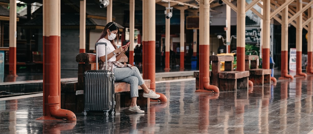 Ragazza adolescente turista asiatica alla stazione ferroviaria che utilizza lo smartphone per la mappa online, il check-in sui social media o la prenotazione del biglietto. Moderna tecnologia dell'app di viaggio, viaggiatore solitario, concetto di avventura ferroviaria per le vacanze estive