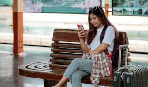 Asiatische Frau wartet auf Zug am Bahnhof. Reisekonzept. Reisender, der das Smartphone für die Online-Reiseplanung verwendet.