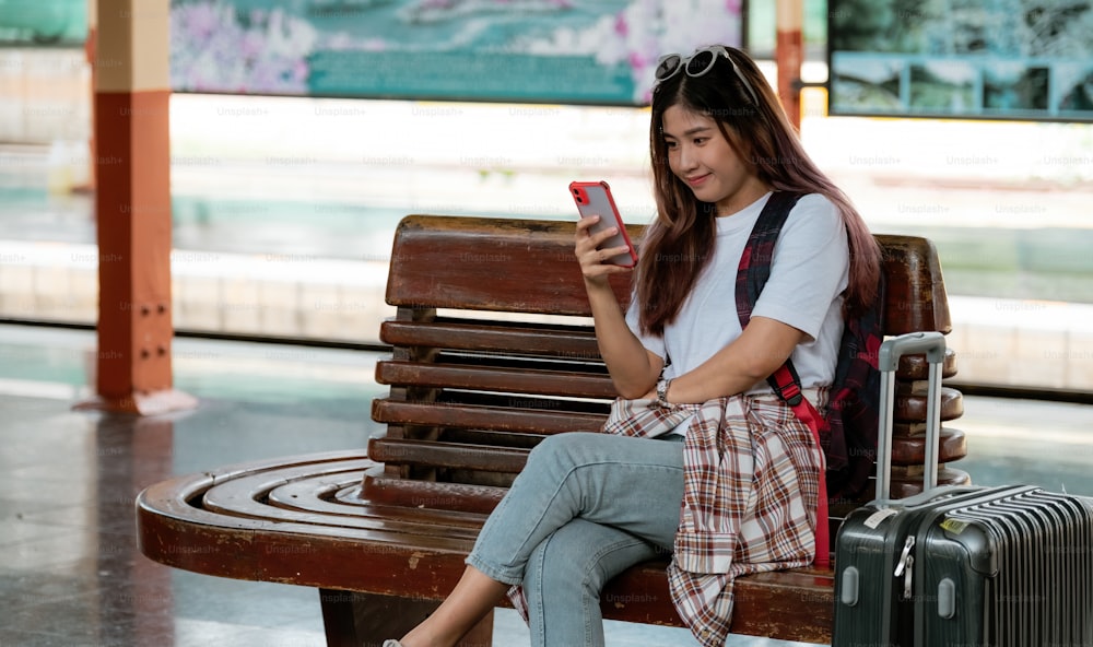 Donna asiatica aspetta il treno sulla stazione ferroviaria. concetto di viaggio. Viaggiatore che utilizza lo smartphone per la pianificazione del viaggio online.