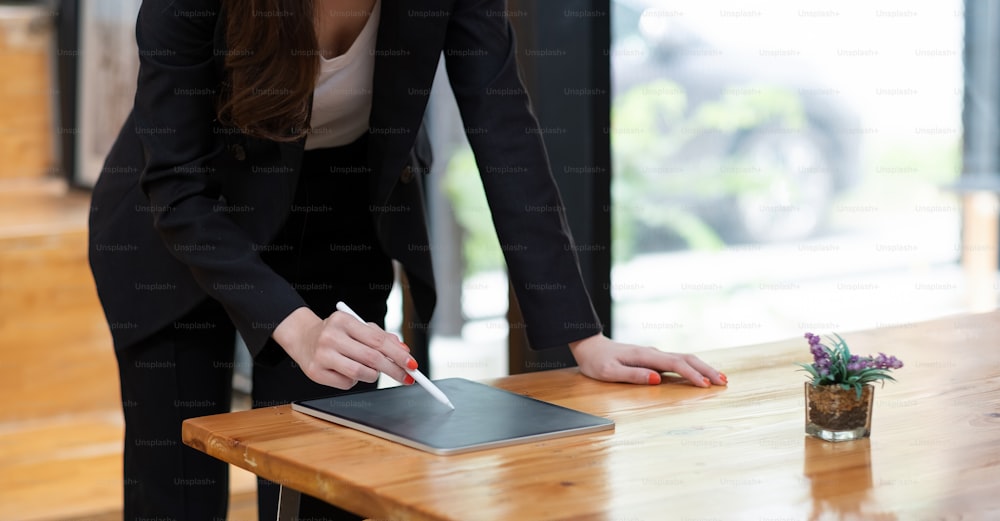 Close up view of business woman holding stylus pen and using digital tablet on wooden desk at cafe