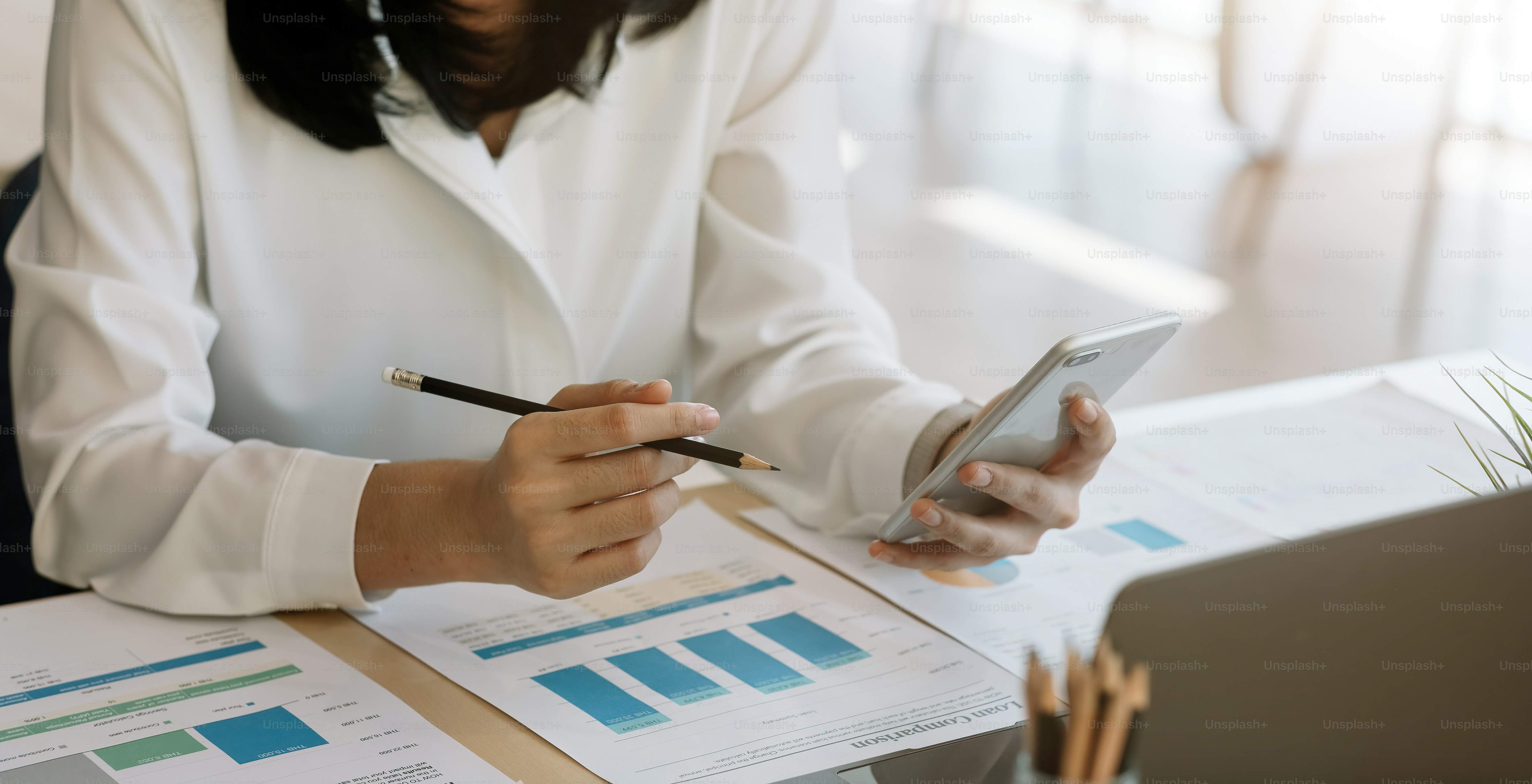 Young woman using smart phone and checking financial report and calculating expenses in the office