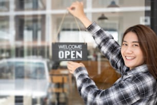 Small business owner turning open sign board on glass window.