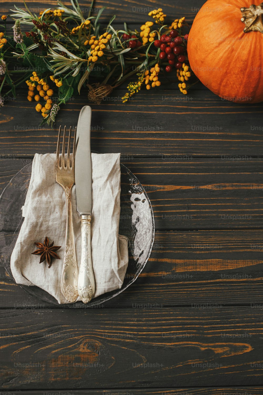 Stilvolle Thanksgiving-Tischdekoration. Moderner Teller mit Vintage-Besteck, Leinenserviette mit Anis auf Holztisch mit Kürbissen und Herbstblumendekoration. Bauernhaus rustikale Herbsthochzeit