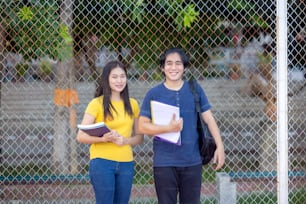 Fora da escola, um jovem casal feliz de estudantes está ao longo de uma cerca, estudando um livro.