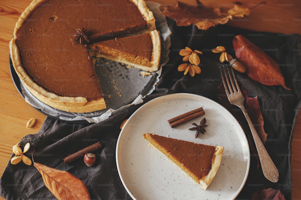 Happy Thanksgiving. Pumpkin pie slice on modern plate on rustic table with linen napkin, autumn leaves, anise and cinnamon. Homemade pumpkin tart recipe. Top view