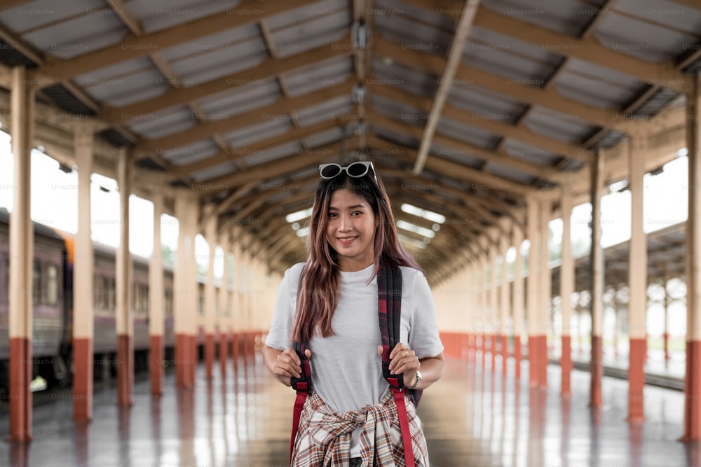 portrait of a young woman traveler with small backpack on the railway stantion. Asian woman backpacker travel alone.