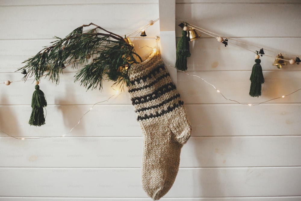 モミの枝とスタイリッシュなガーランドとクリスマスライト付きの白い木製の壁にクリスマスの素朴なストッキング。華やかな内装の雰囲気のあるスカンジナビアの客室です。モダンな手作りの装飾