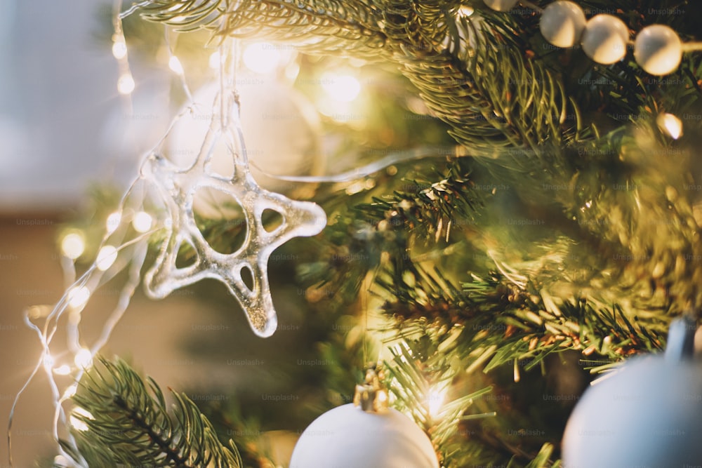 현대 유리 크리스마스 장식품, 나무 화환, 흰색 싸구려 및 황금 크리스마스 조명이 닫힙니다. 분위기 있는 축제 장식 스칸디나비아 객실. 세련된 크리스마스 장식, 유리 별
