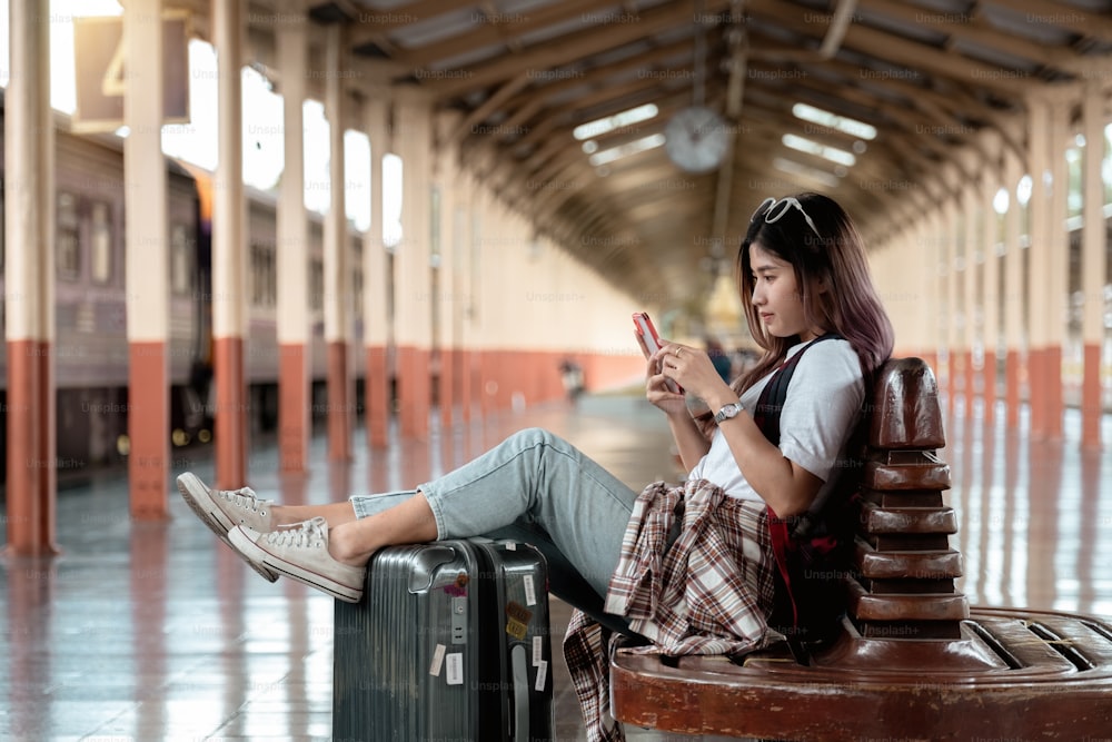 La donna asiatica è viaggiatrice, sta aspettando il loro treno. Ragazza che usa lo smartphone al concetto di viaggio di avventura all'aperto in treno.