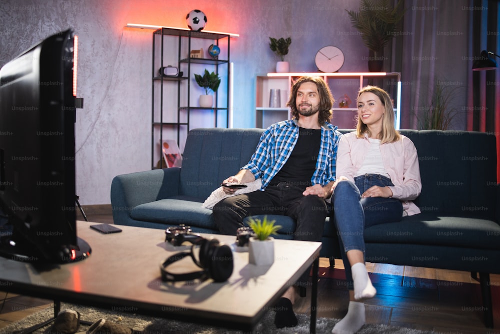 Pleasant lovely couple of young people relaxing together on cozy sofa and watching television at home. Concept of leisure time and recreation.