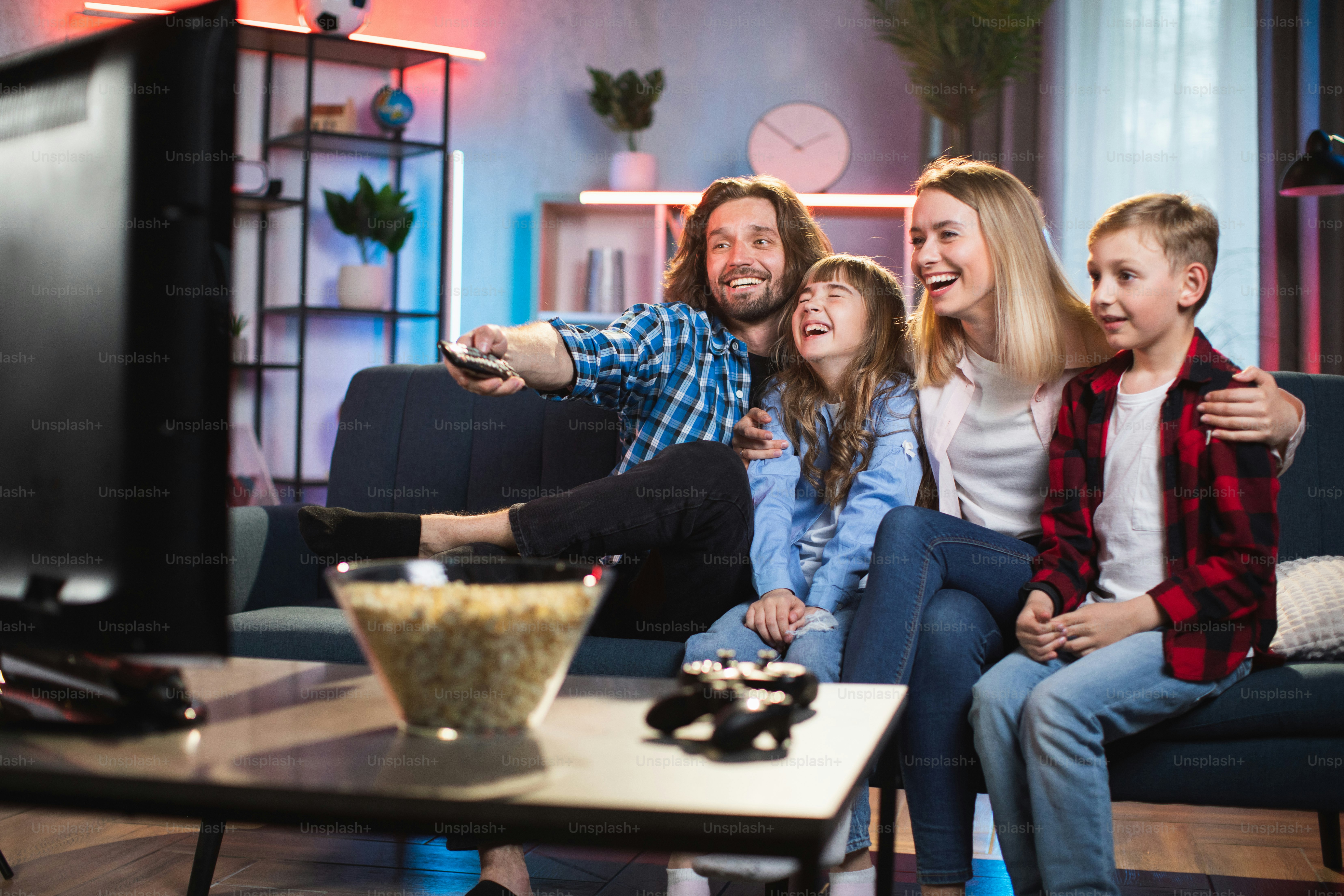 A family on a sofa watching television with a bowl of popcorn
