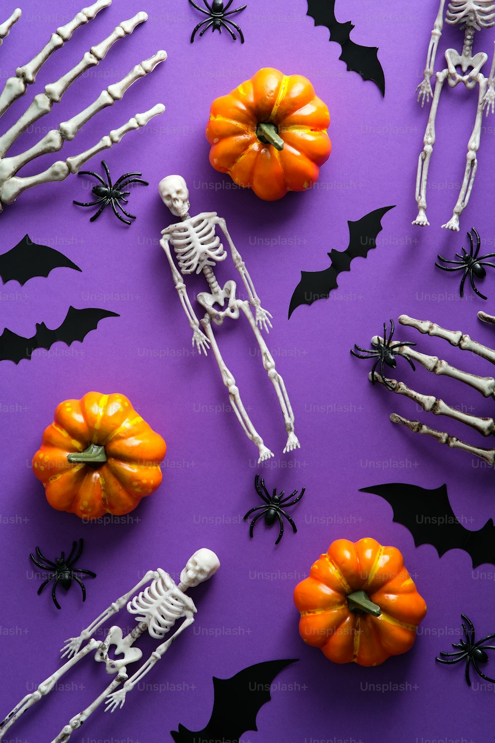 Happy Halloween holiday concept. Flat lay, top view pumpkins, skeletons, bats, spiders on purple background.