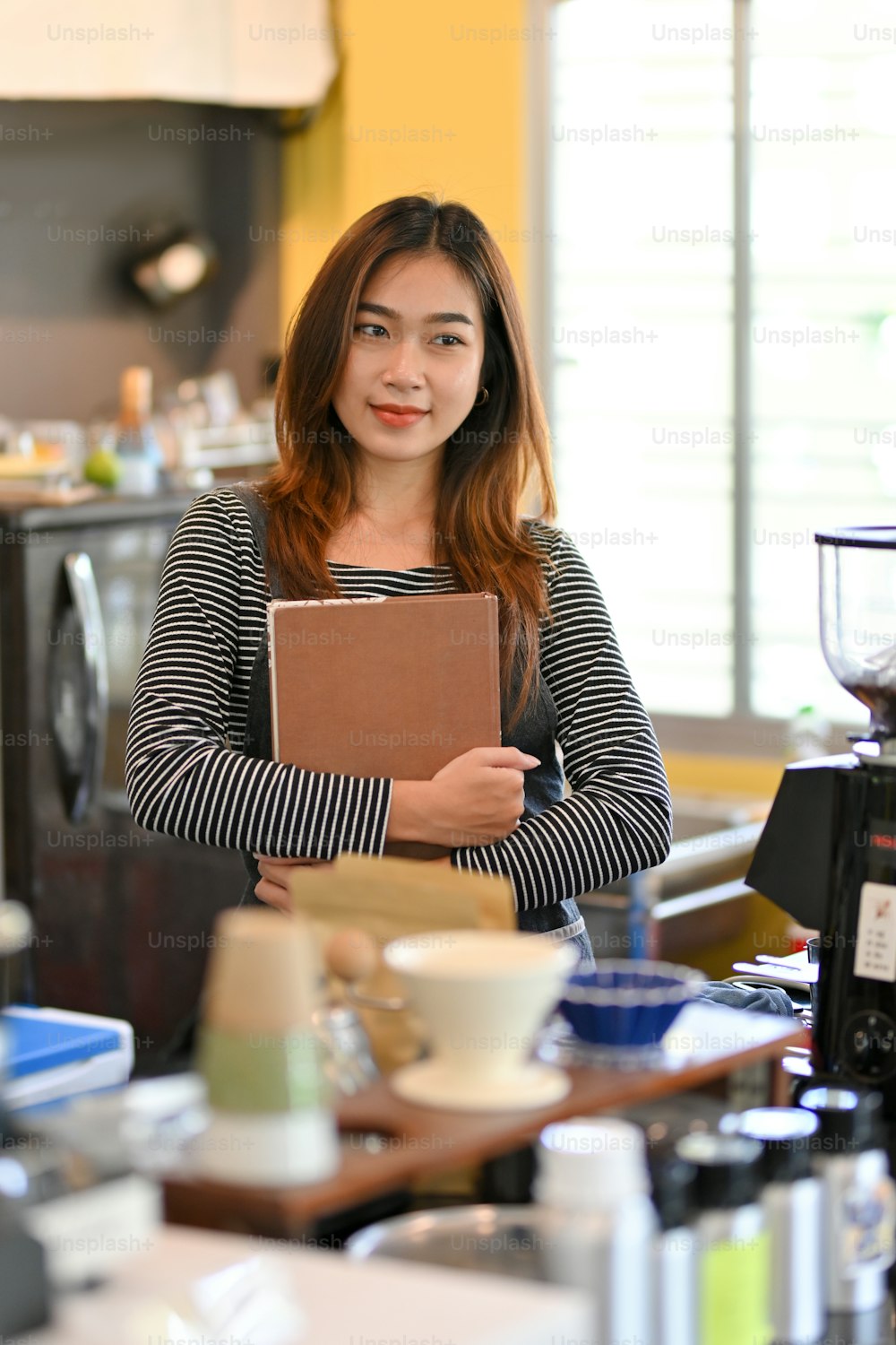 Portrait of cheerful female barista smiling, looking away, standing near coffee machine at coffee shop